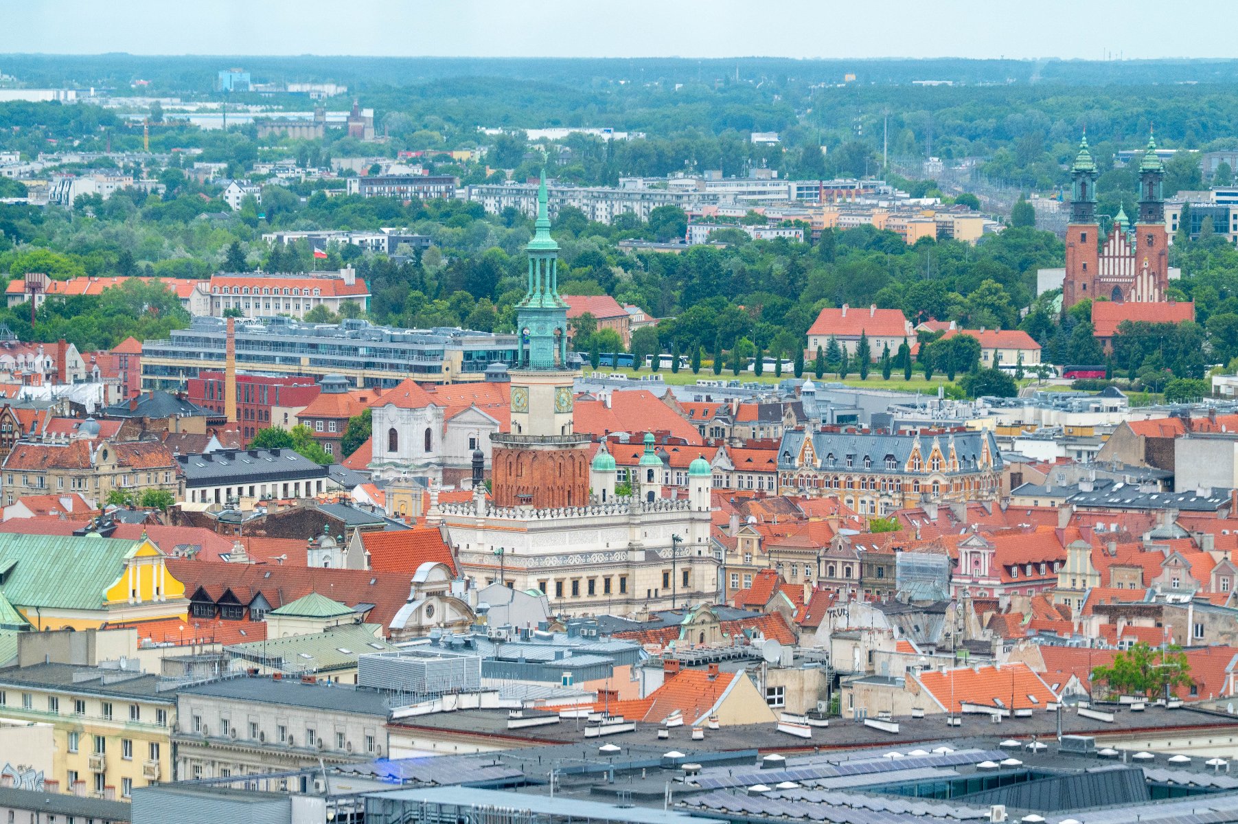 Widok z góry na panoramę Poznania z wyraźnie widoczną wieżą Ratusza na Starym Rynku oraz wieżami Katedry w tle po prawej stronie.