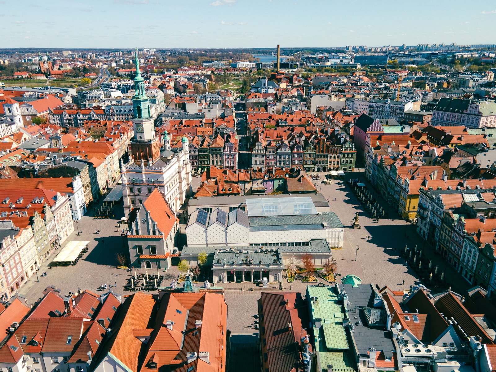 Widok z lotu ptaka na centrum miasta. W centrum rozległy plac otoczony budynkami z czerwonymi dachami. Na placu charakterystyczny budynek z zieloną wieżą, prawdopodobnie obiekt historyczny.