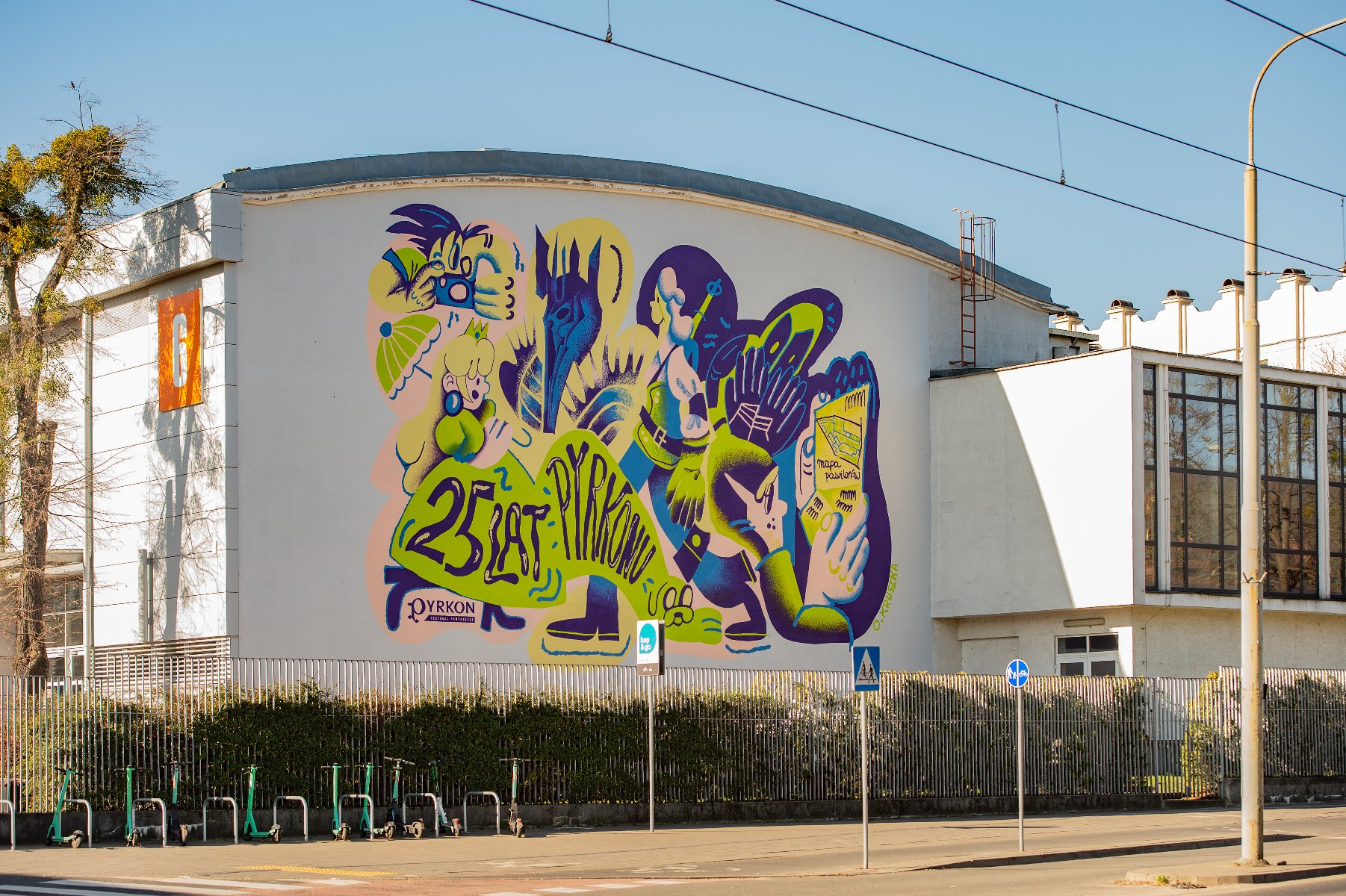 Wielki mural z wizerunkiem różnych fantastycznych postaci i napisem "25 lat Pyrkonu", umieszczony na ścianie jednego z budynków MTP.