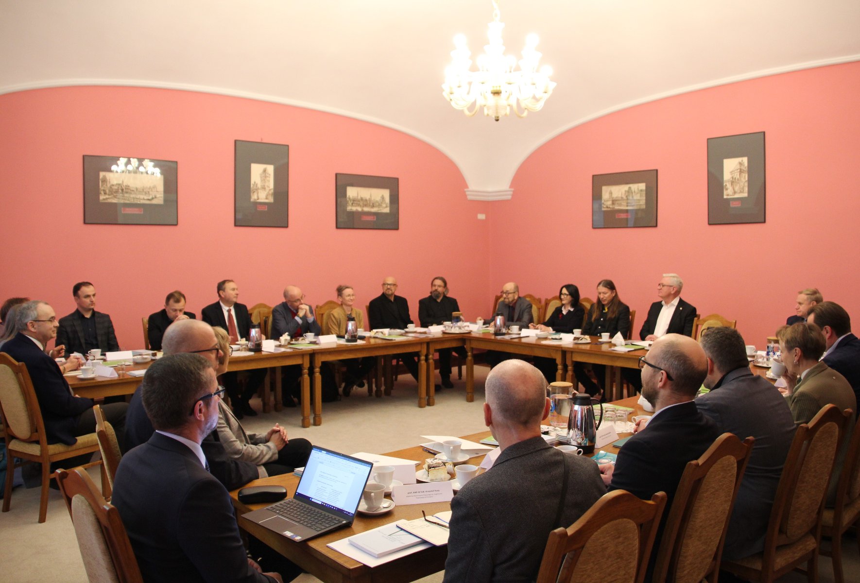 Wioczna cała sala Malinowa, na ścianach grafiki w ramkach. Przy długim, drewnianym stole w kształcie podkowy siedzą naukowcy i naukowczynie w uoczystych strojach. Na szczycie stołu jest prezydent Jaśkowiak.