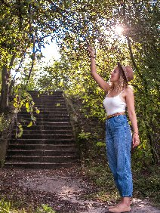 Kobieta stoi w parku i przygląda się zielonym gałązkom.