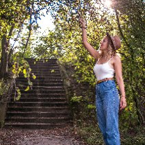 Kobieta stoi w parku i przygląda się zielonym gałązkom.