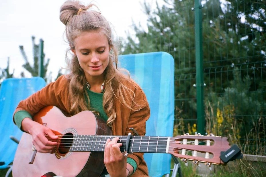 Zdjęcie Julii Pietruchy z gitarą. Artystka siedzi na niebieskim wysokim leżaku, w tle drzewa.