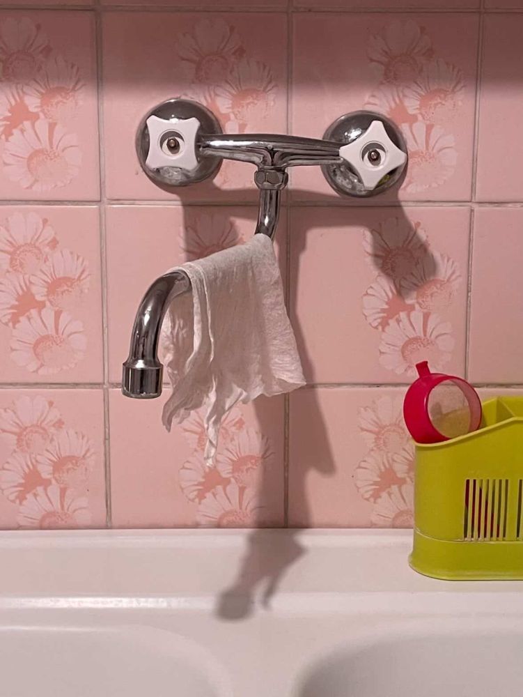 Zdjęcie kuchennego zlewu z metalowym kranem i wiszącą na nim ścierką.