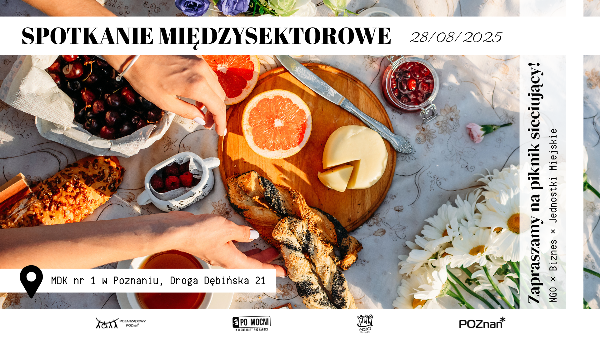 Zdjęcie poczęstunku w formie pikniku, na rozłożonym obrusie owoce, pieczywo, filiżanka herbaty i bukiet kwiatów i sięgajace po jedzenie dłonie