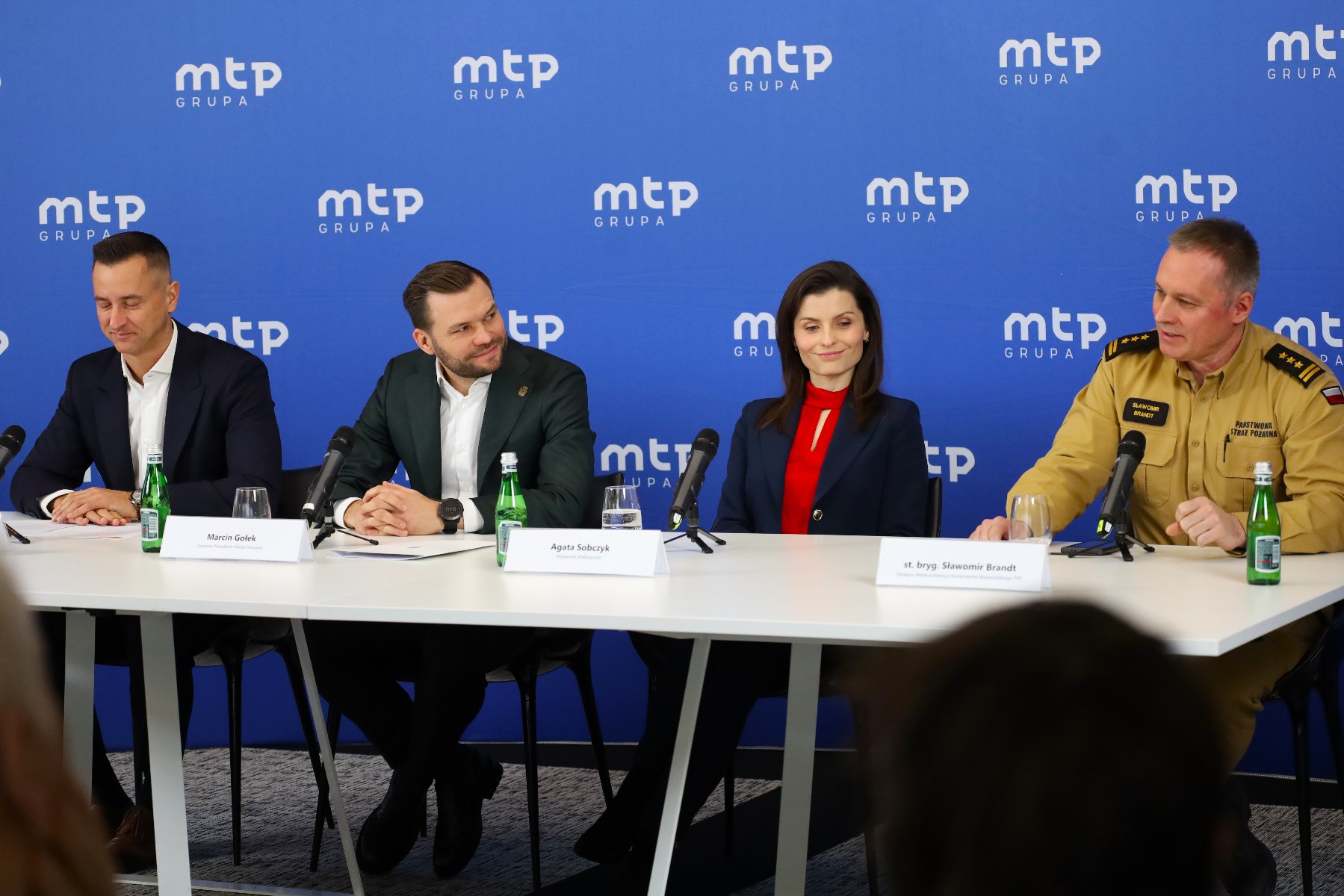 Zdjęcie przedstawia cztery osoby siedzące za stołem przed mikrofonami - jedną kobietę i trzech mężczyzn.