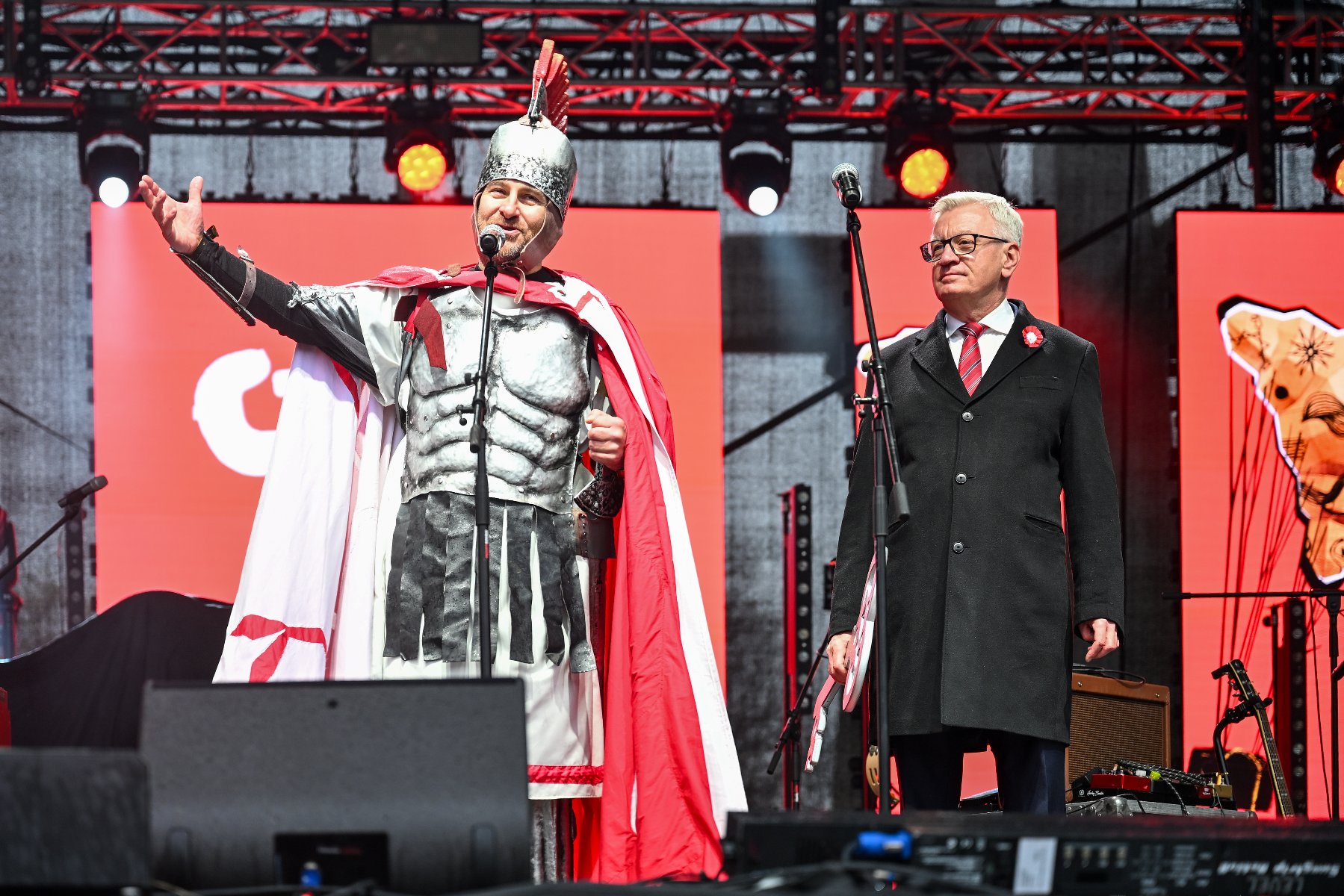 Zdjęcie przedstawia dwóch mężczyzn na scenie podczas przekazania kluczy. Jeden w przebraniu rycerza.