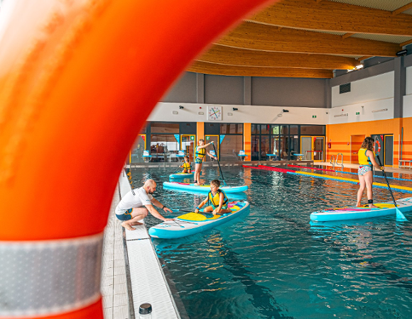 Zdjęcie przedstawia dzieci pływające na deskach w basenie.