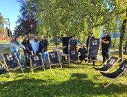 Zdjęcie przedstawia grupę młodych ludzi, którzy pokazują rękami na leżaki. Wokół nich jest zieleń.