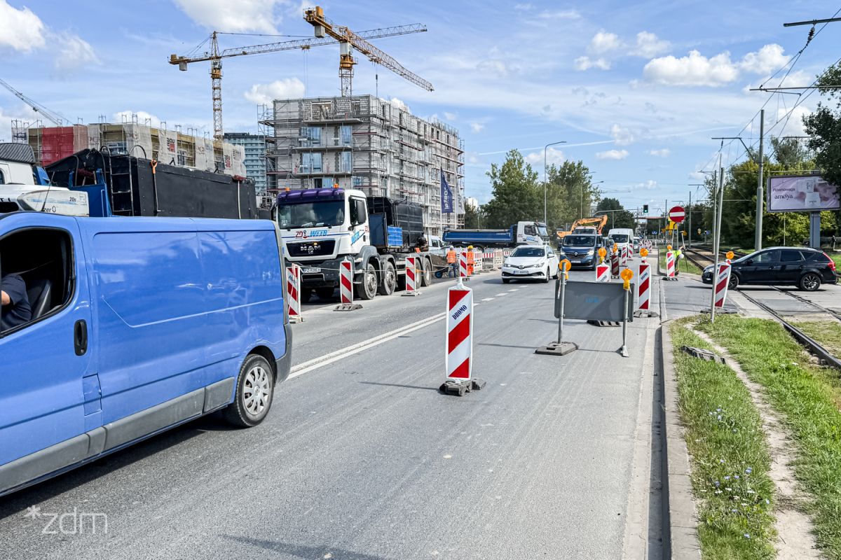 Zdjęcie przedstawia jezdnię, na której stoją pachołki wyznaczające objazdy. Pomiędzy nimi jeżdżą samochody.