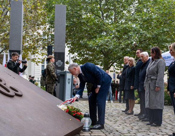 Zdjęcie przedstawia ludzi stojących przed pomnikiem.