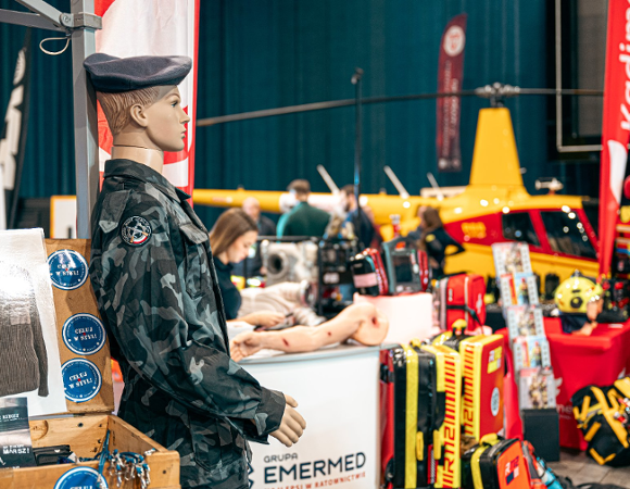 Zdjęcie przedstawia manekina w mundurze wojskowym. W tle widać między innymi helikopter oraz sztuczną rękę.