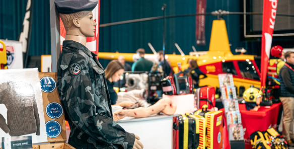 Zdjęcie przedstawia manekina w mundurze wojskowym. W tle widać między innymi helikopter oraz sztuczną rękę.