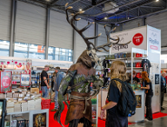 Zdjęcie przedstawia młodą osobę stojącą na przeciwko człowieka przebranego za Leszego. W tle widać stoiska z książkami i ludzi.