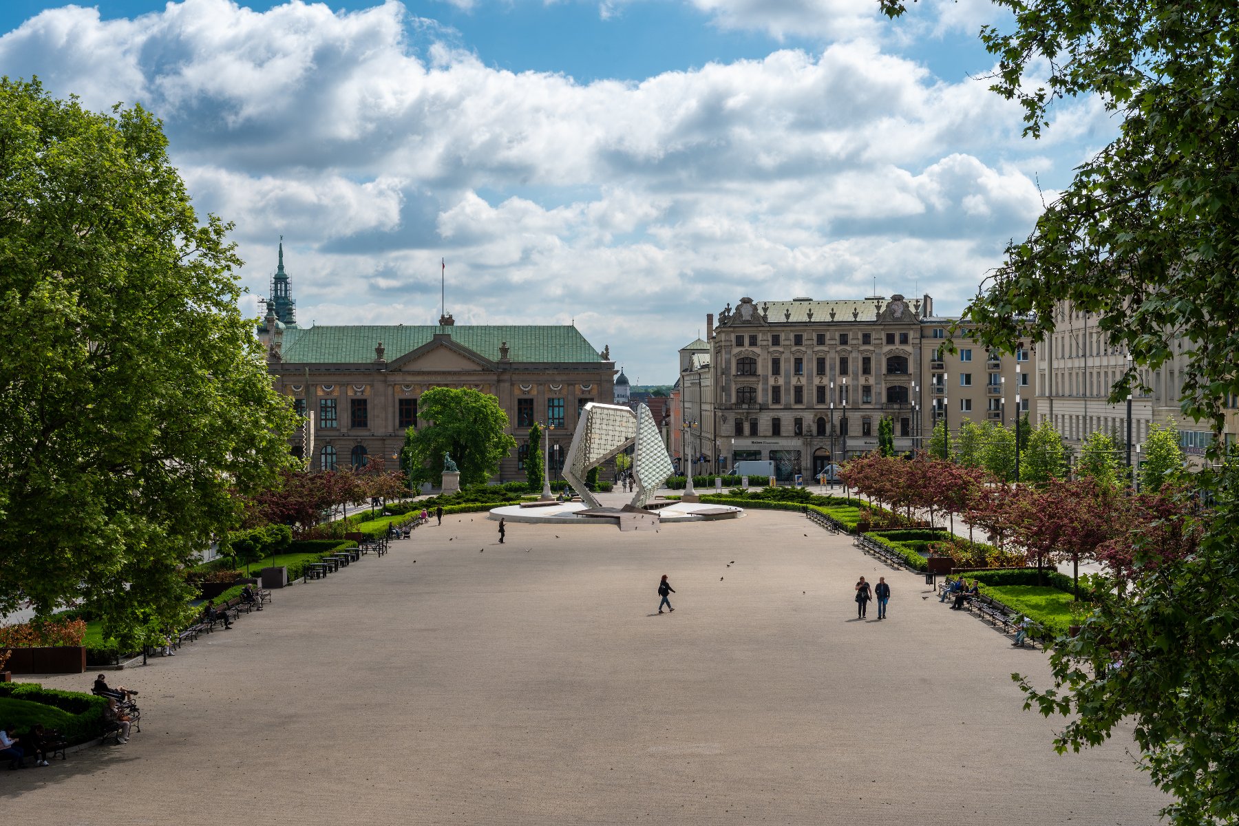 Zdjęcie przedstawia Plac Wolności oraz otaczające go drzewa i budynki.