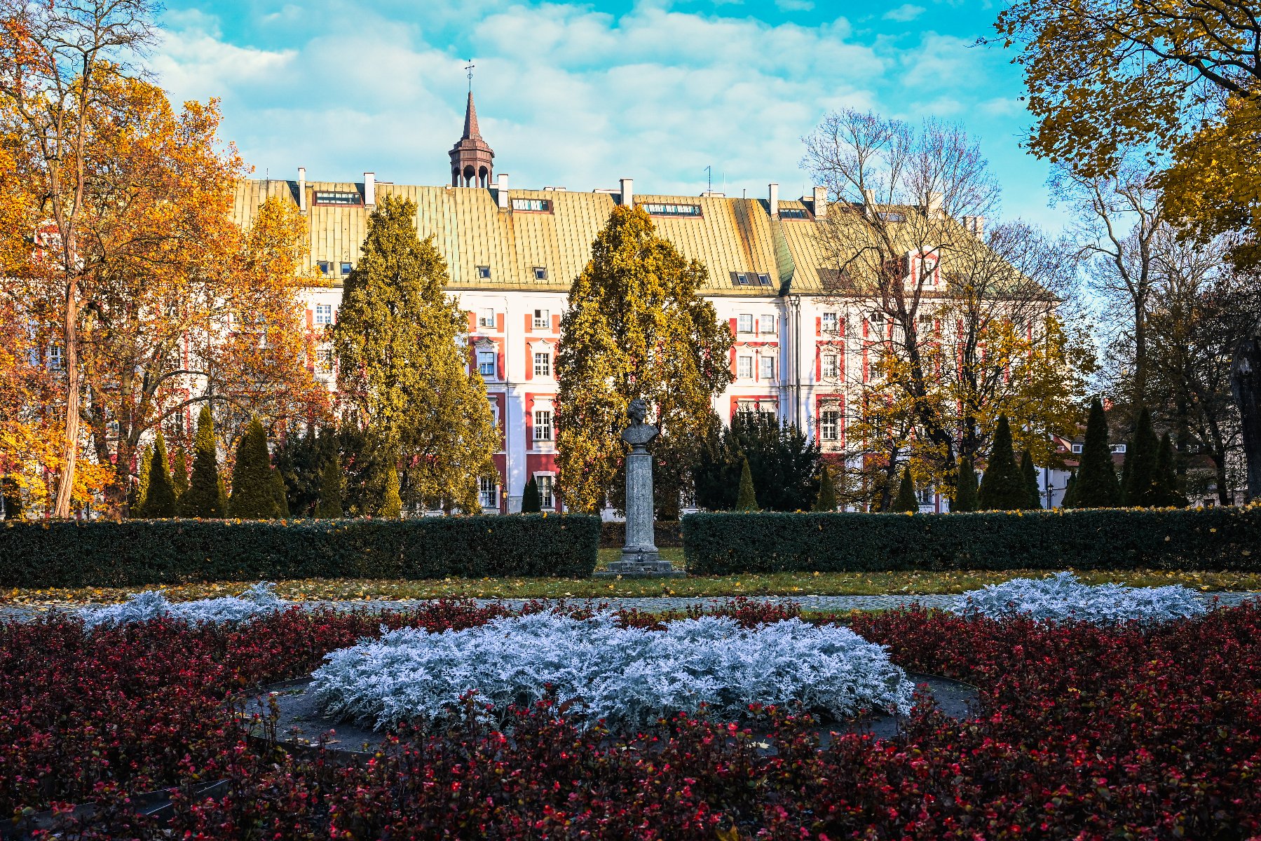 Zdjęcie przedstawia popiersie Chopina. W tle widać drzewa w jesiennych, złotych barwach.
