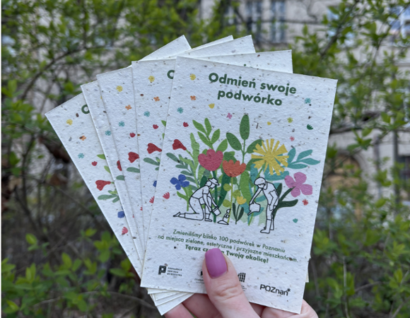 Zdjęcie przedstawia rękę, która trzyma ulotki z napisem "Odmień swoje podwórko" i rysunkiem osób sadzących kwiaty.