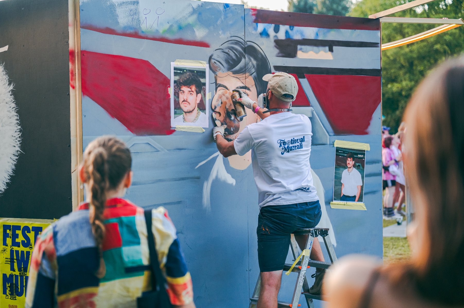 Zdjęcie przedstawia rękę trzymającą ulotki zapowiadające festiwal. W tle widać ściankę z muralem.