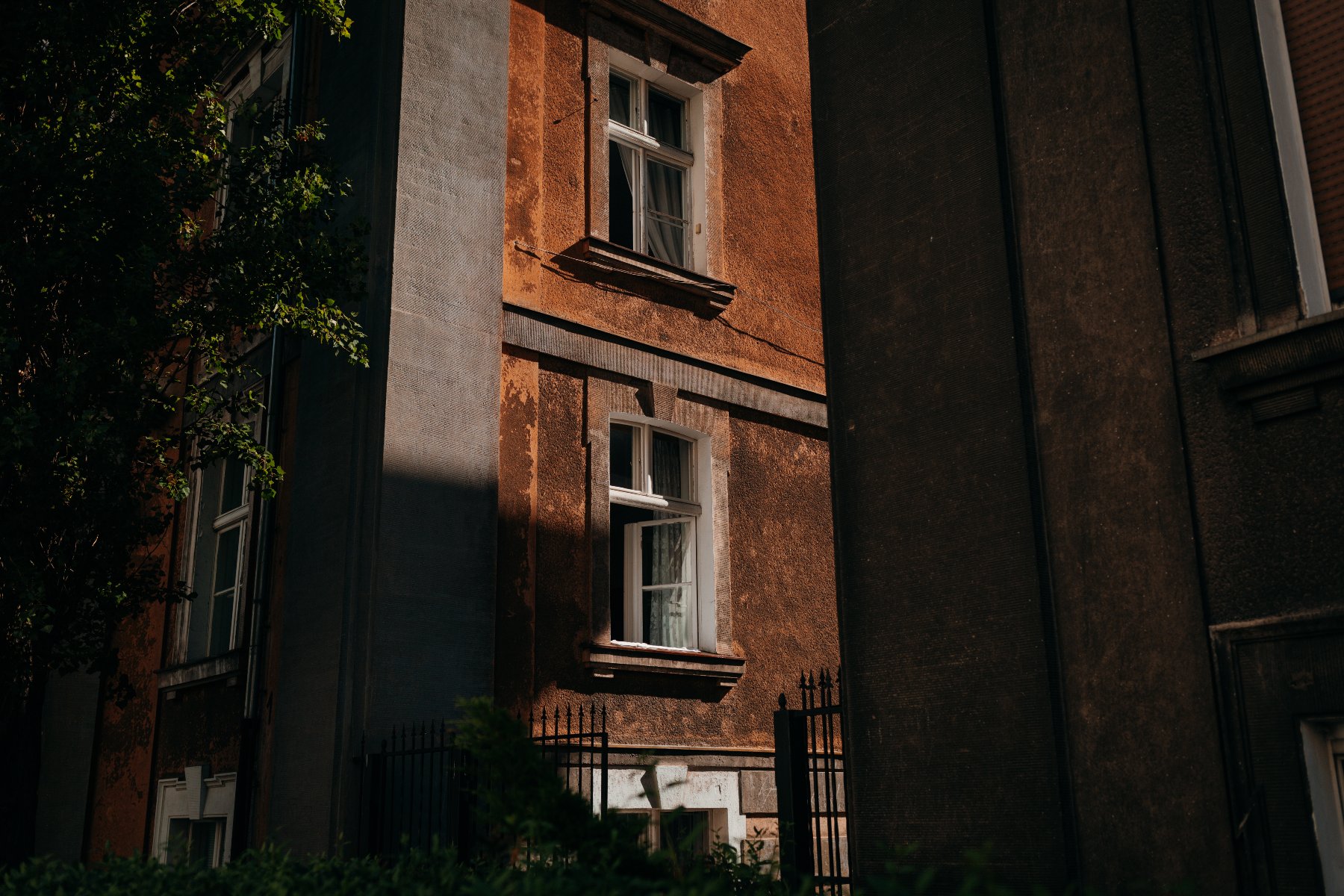 Zdjęcie przedstawia róg kamienicy. Znajdują się na nim stare drewniane okna.