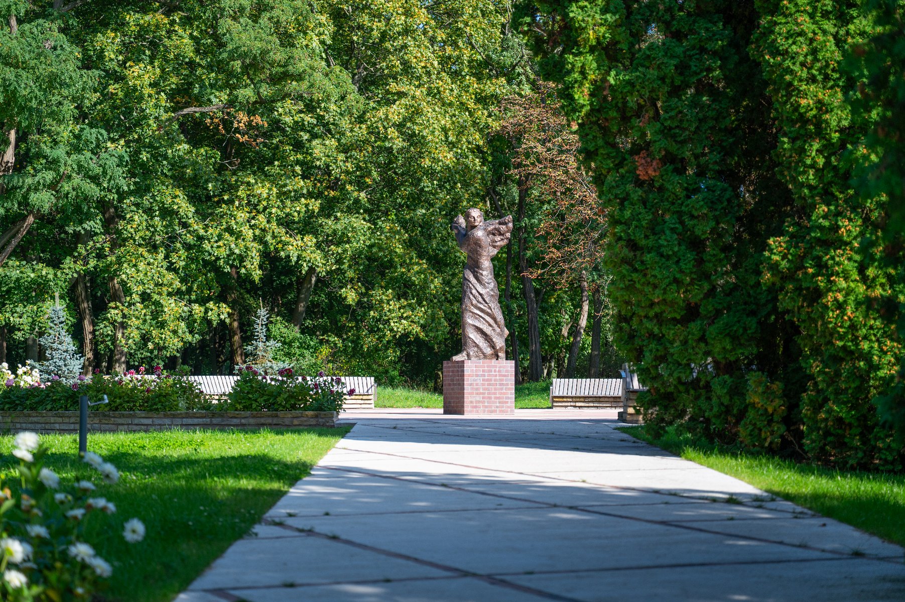 Zdjęcie przedstawia rzeźbę wśród zieleni oraz mężczyznę robiącego jej zdjęcie.