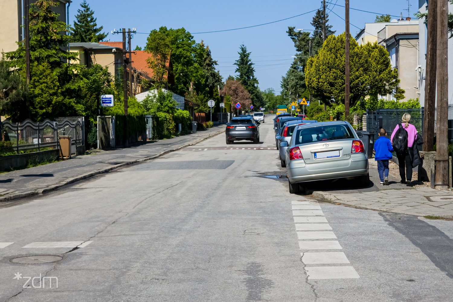 Zdjęcie przedstawia samochody zaparkowane na poboczu ulicy. Jedno z aut ma blokadę na kołach.