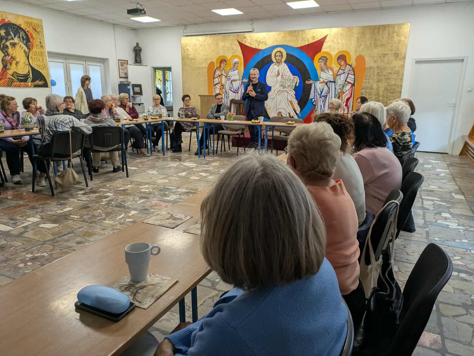 Zdjęcie przedstawia spotkanie seniorów z przedstawicielami władz miasta. Uczestnicy siedzą przy stołach.