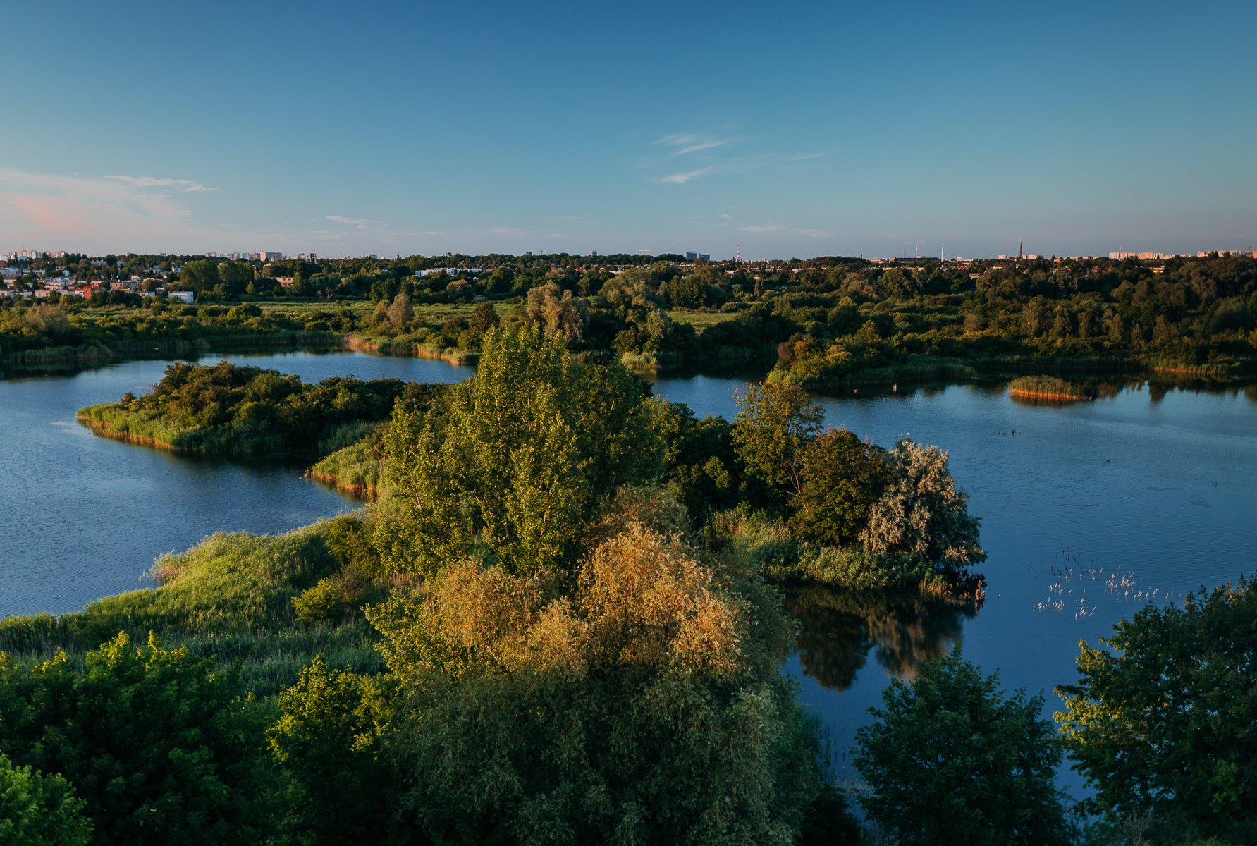 Zdjęcie przedstawia stawy otoczone zielenią. Zdjęcie z lotu ptaka.