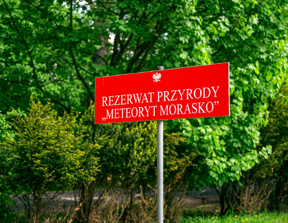 Zdjęcie przedstawia tabliczkę z nazwą rezerwatu wśród zieleni.