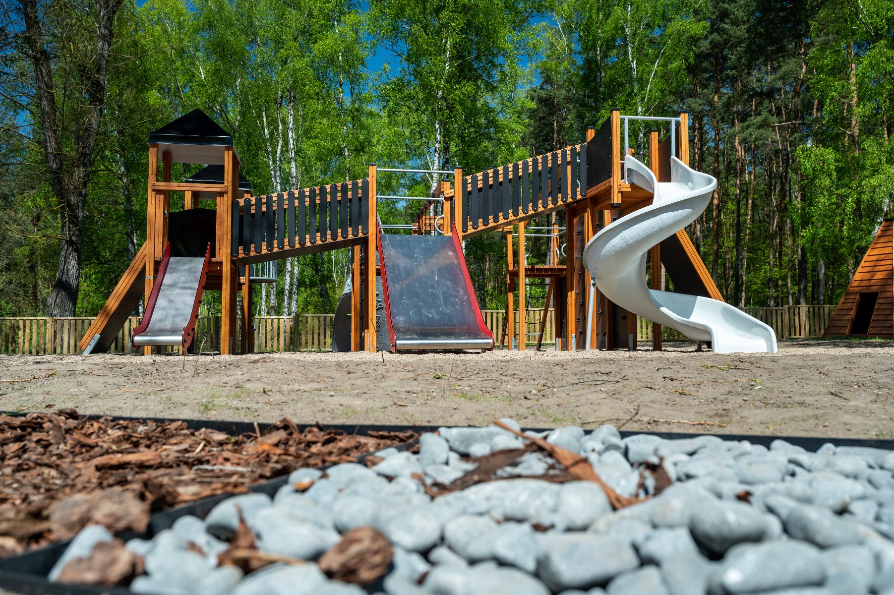Zdjęcie przedstawia tłum ludzi na plaży. Niektórzy spacerują, inni leżą, jeszcze inni jeżdżą na rowerach. W tle widać jezioro.