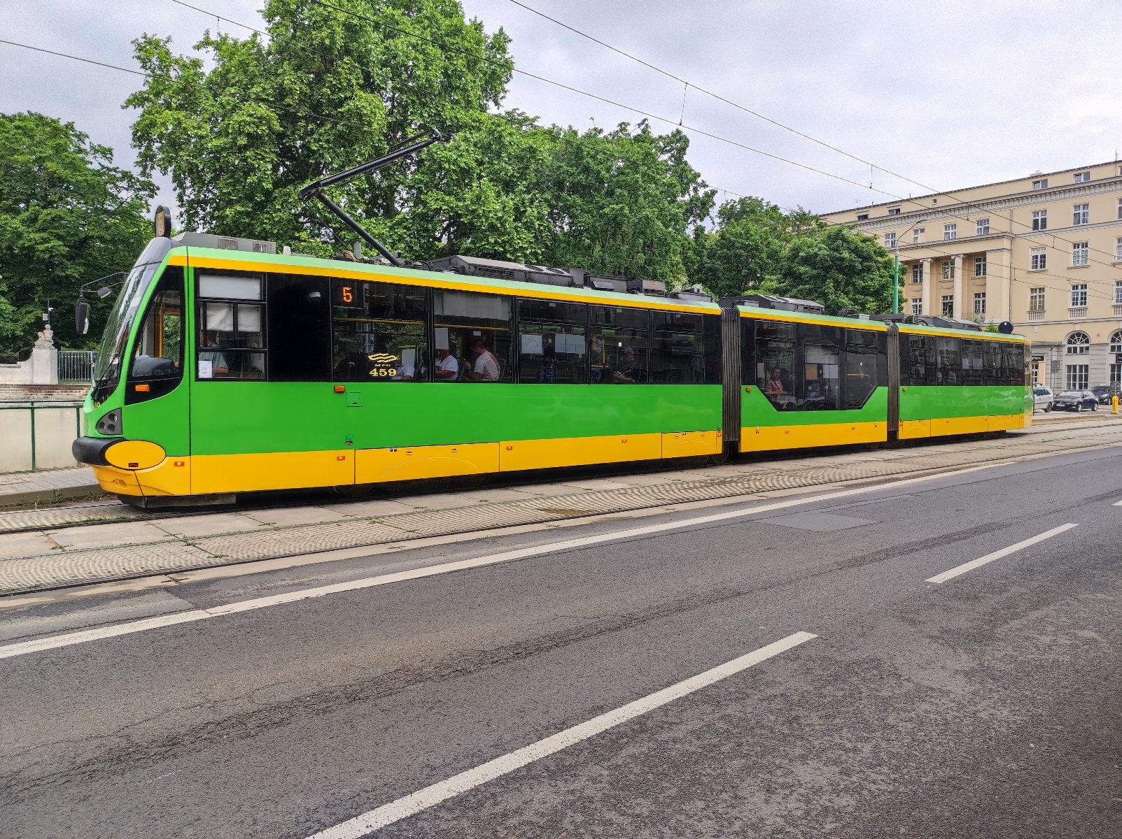 Zdjęcie przedstawia tramwaj numer 5 w kolorze zielono-żółtym.