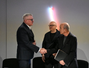 Zdjęcie przedstawia trzech mężczyzn. Dwóch podaje sobie ręke.