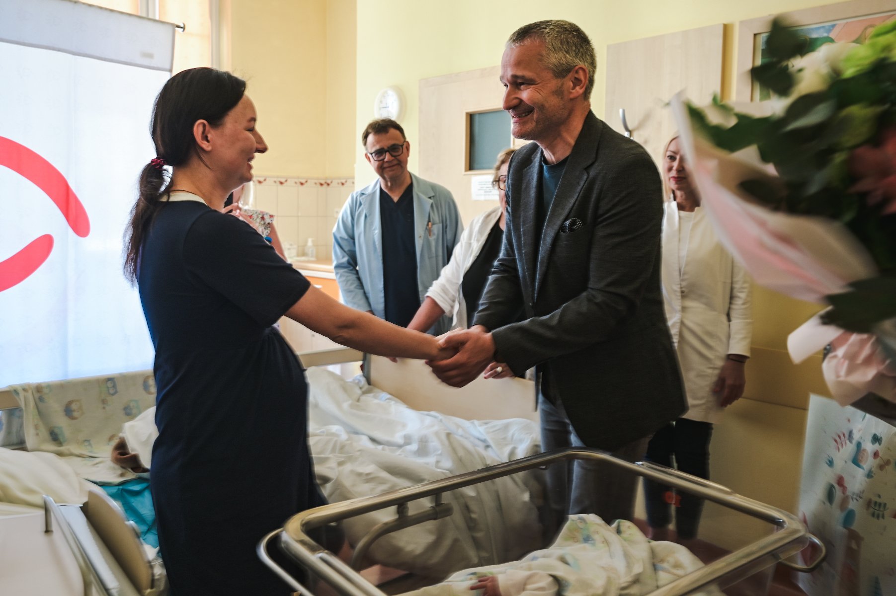 Zdjęcie przedstawia wiceprezydenta ściskajacego rękę młodej kobiecie w szpitalnej sali. Za jego plecami stoją lekarze.