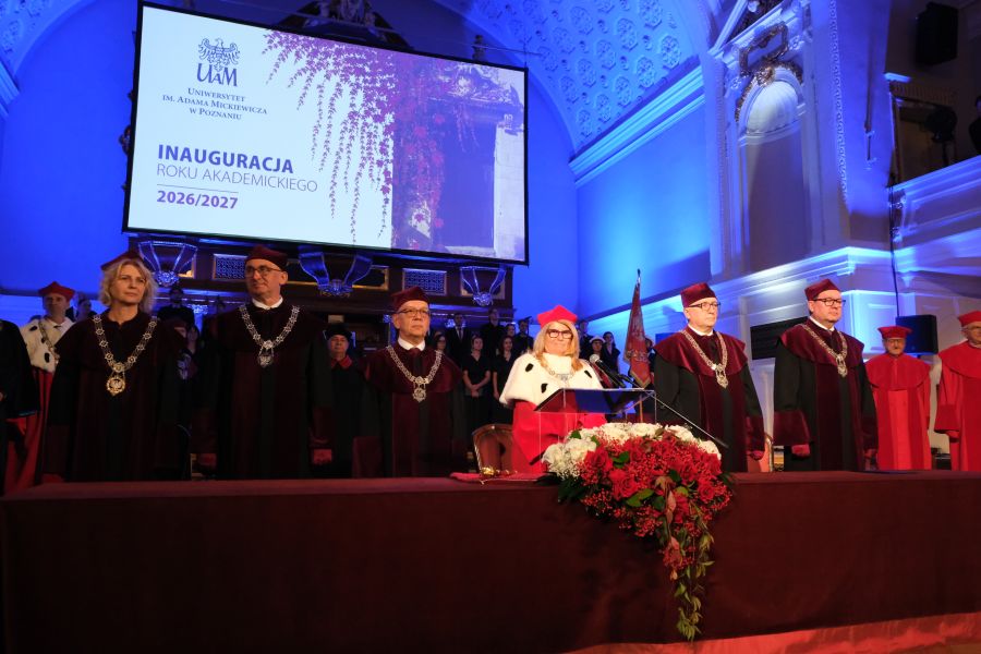 Zdjęcie przedstawia władze uczelni stojących za stołem w auli w togach.