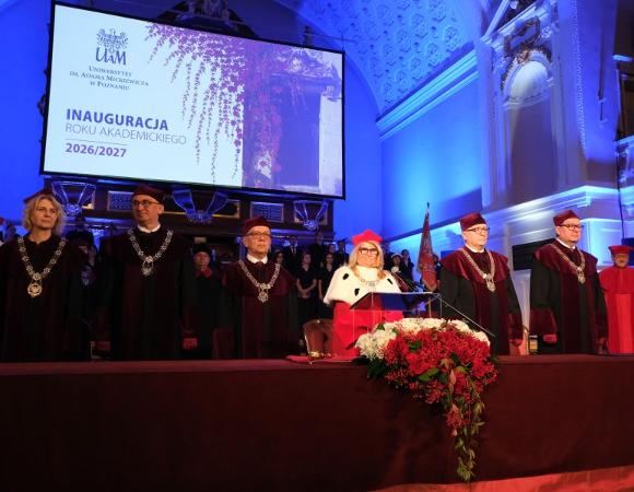 Zdjęcie przedstawia władze uczelni stojących za stołem w auli w togach.