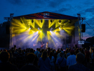 Zdjęcie rozświetlonej sceny podczas koncertu i publiczność stojąca przed nią