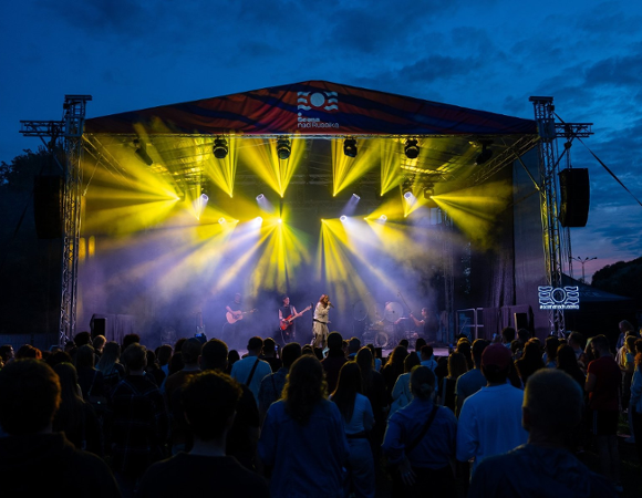 Zdjęcie rozświetlonej sceny podczas koncertu i publiczność stojąca przed nią