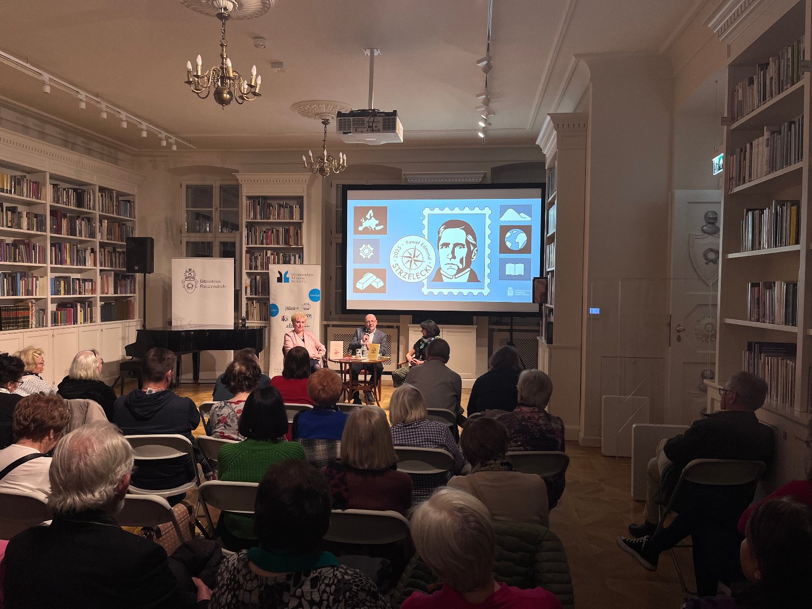 Zdjęcie ukazuje moderatorkę i autorów książki oraz przybyłych na spotkanie mieszkańców