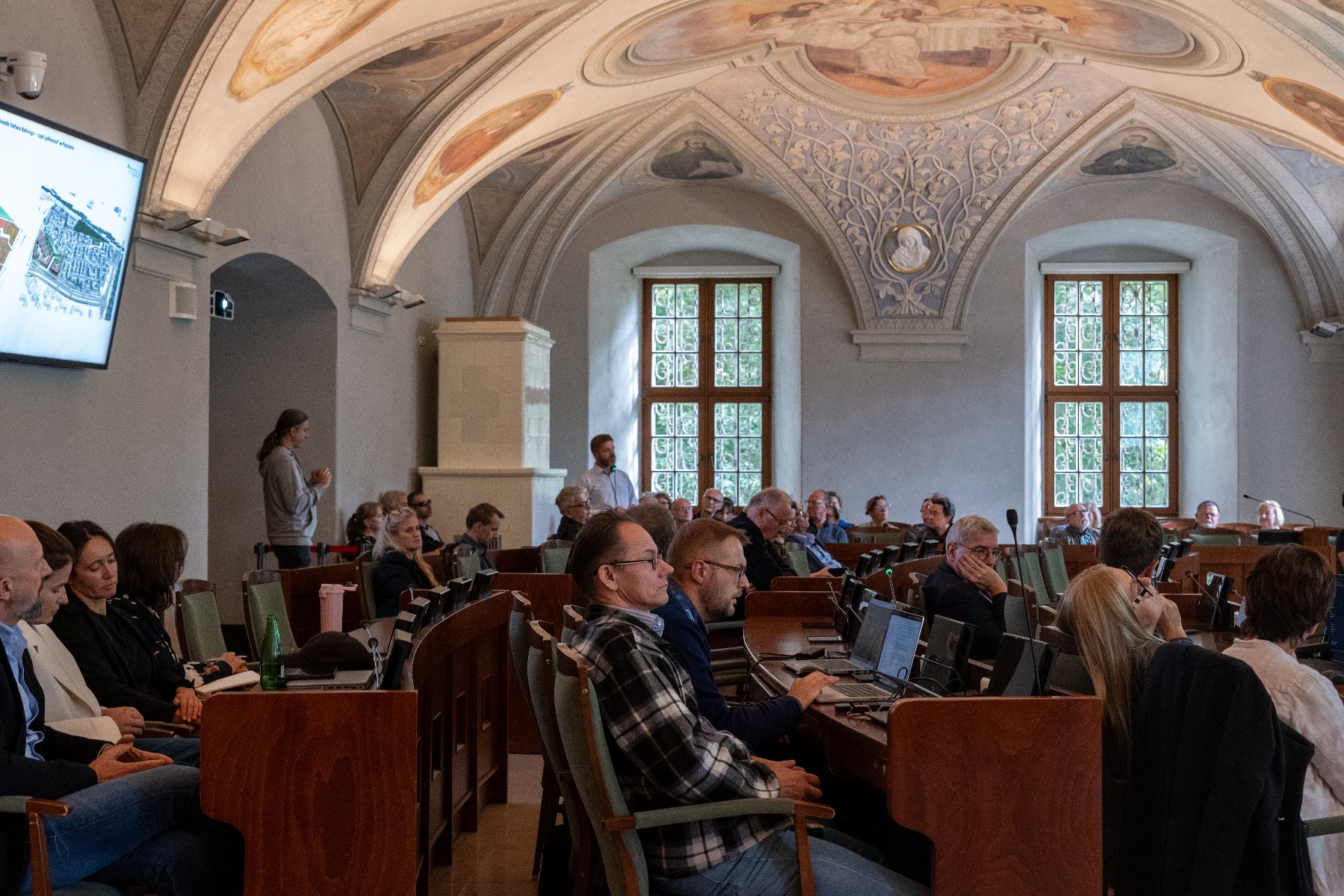 Zdjęcie z obrad komisji. W sali siedzi kilkadziesiąt osób, na ekranie wyświetlany jest plan - mapa.