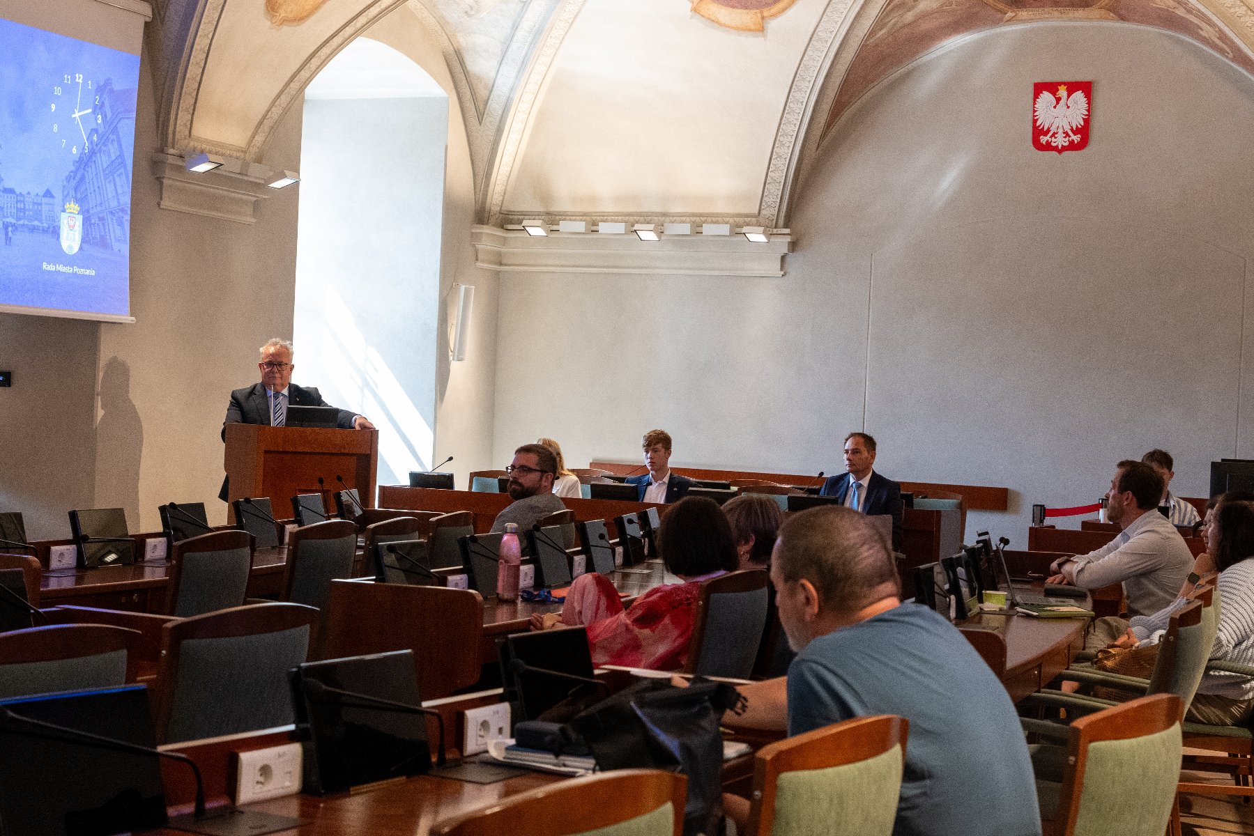 Zdjęcie z sali obrad. Radni i goście siedzą przy lożach.