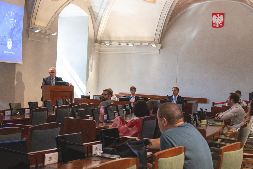 Zdjęcie z sali obrad. Radni i goście siedzą przy lożach
