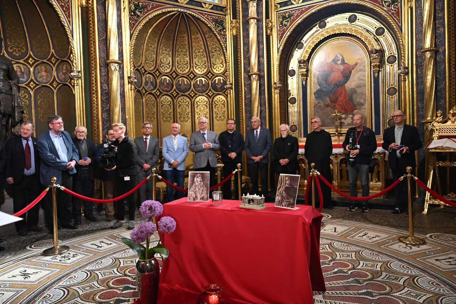 Zdjęcie z uroczystości. Uczestnicy stoją w złotej kaplicy wokół stołu z relikwiami.