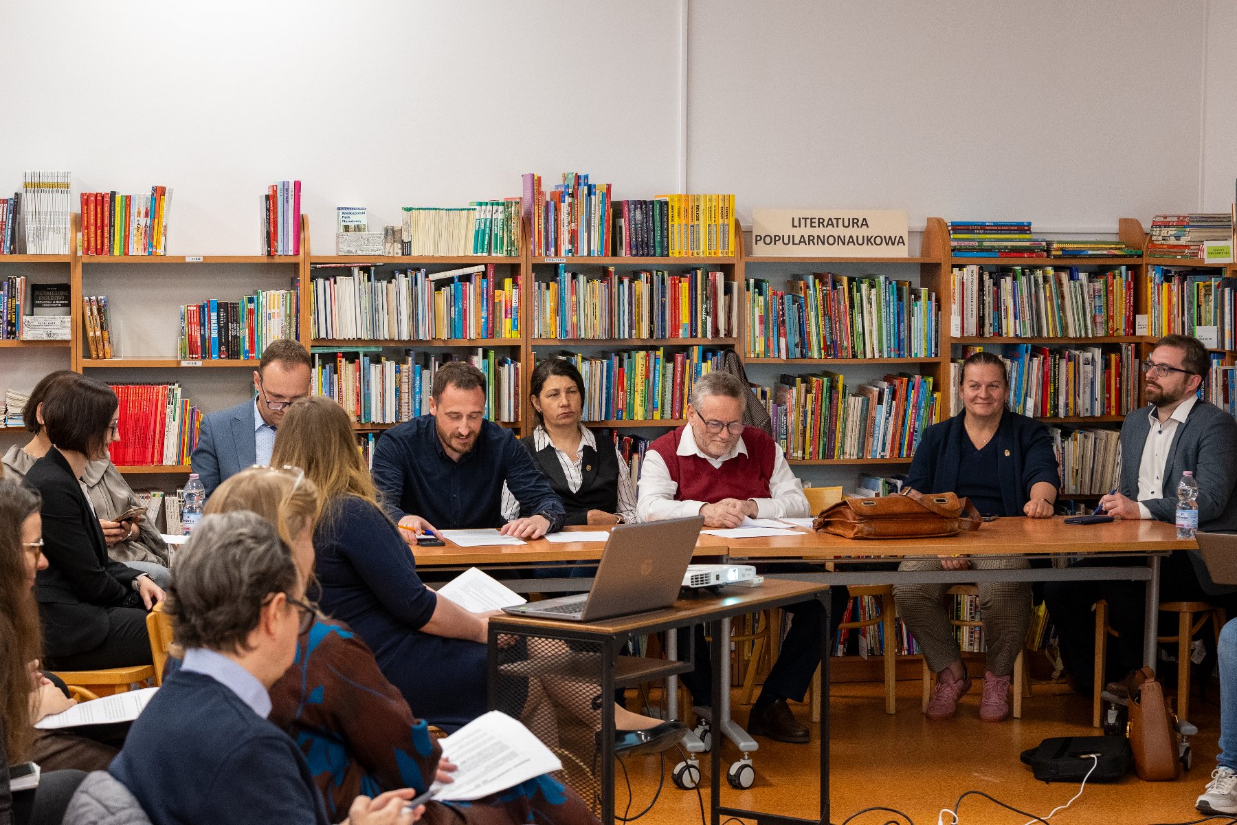 Zdjęcie zostało wykonane w bibliotece. Radni siedzą przy stole, na tle książek.