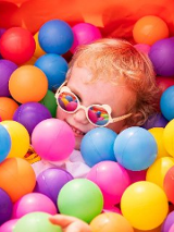 Uśmiechnięte dziecko znajdujące się wśród kolorowych, plastikowych kulek.