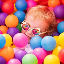 Uśmiechnięte dziecko znajdujące się wśród kolorowych, plastikowych kulek.