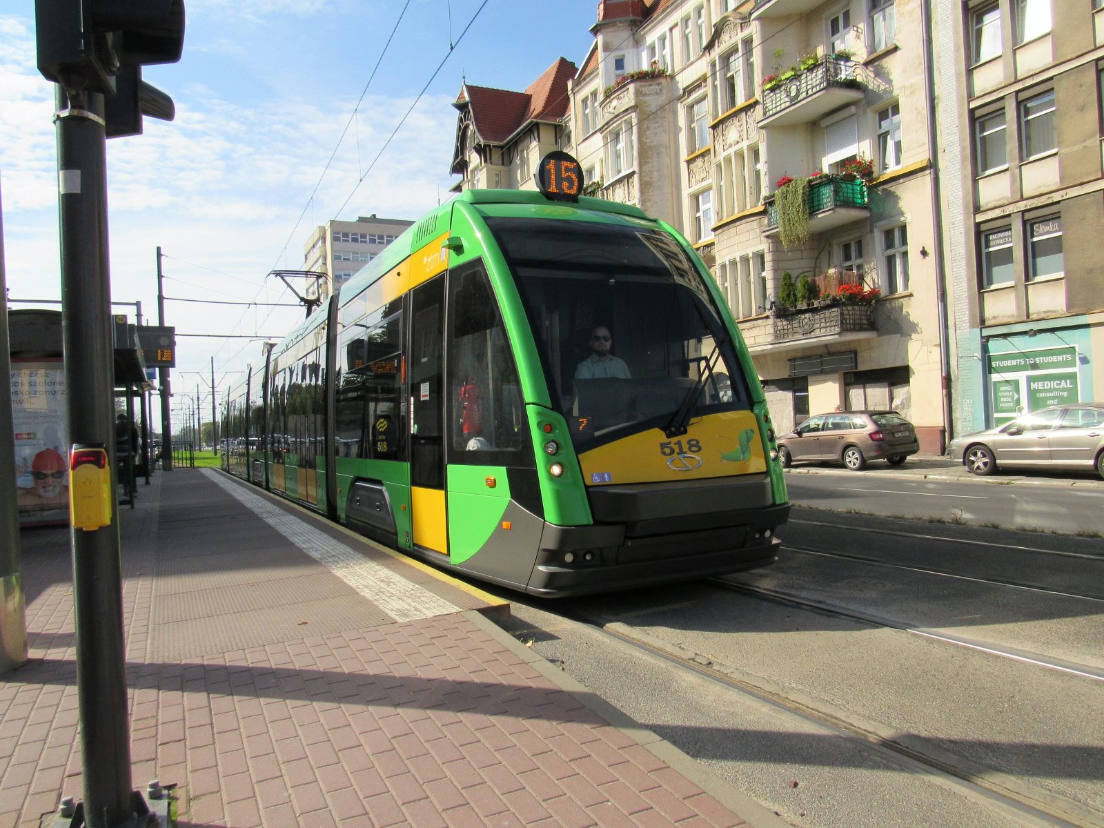 Zielono żółty tramwaj na przystanku, w tle kamienice
