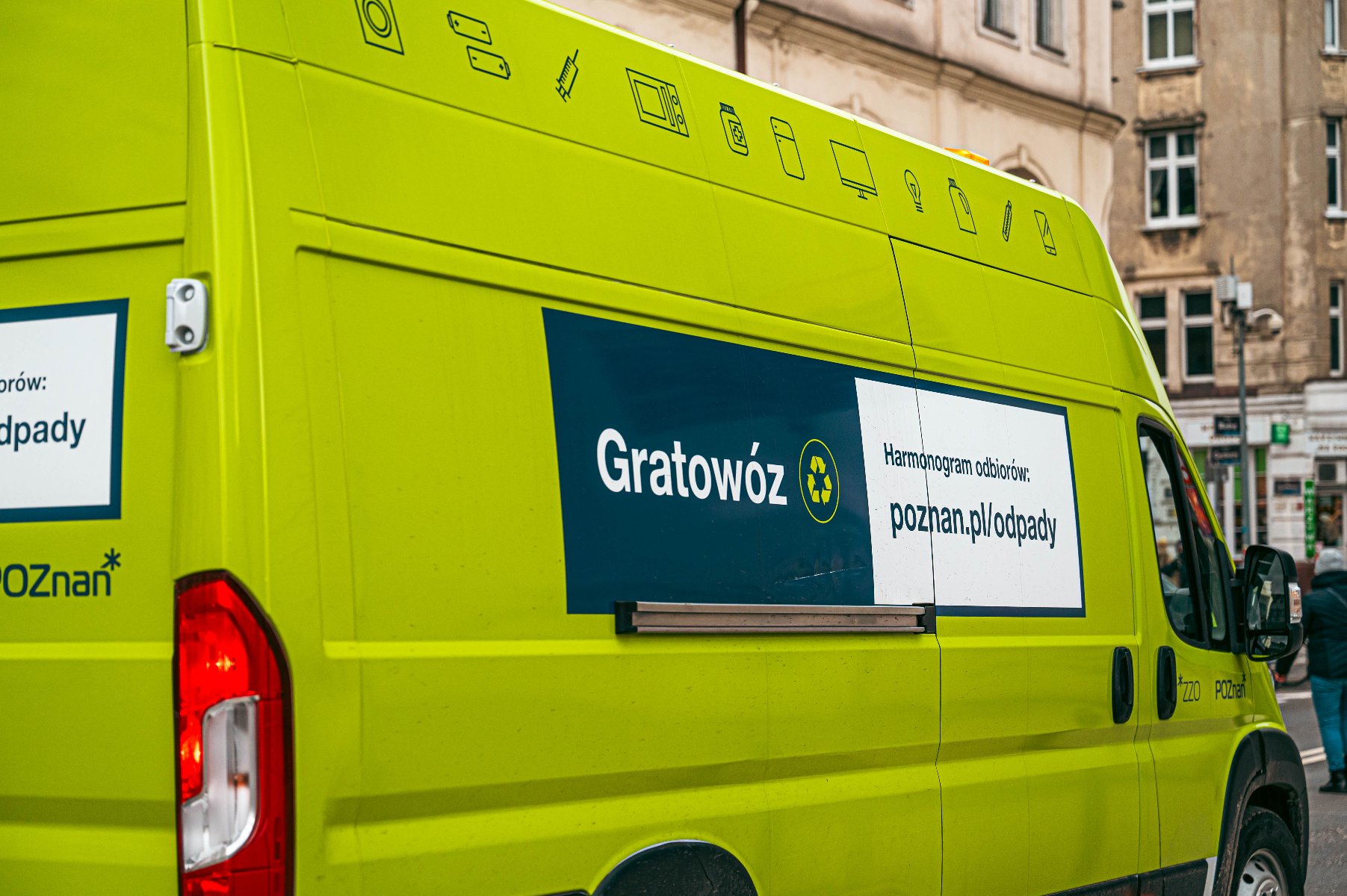 Zielony bus zaparkowany na miejskiej ulicy. Na jego boku znajduje się napis: "Gratowóz" oraz symbol recyklingu. Poniżej widnieje tekst: "Harmonogram odbiorów: poznan.pl/odpady".