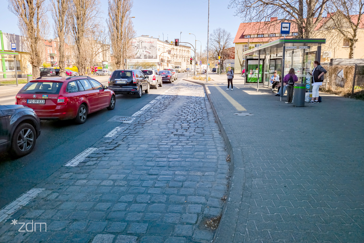 Zniszczona zatoka przystankowa przy ul. Głównej, po lewej jezdnia z samochodami czekającymi przed sygnalizacją świetlną