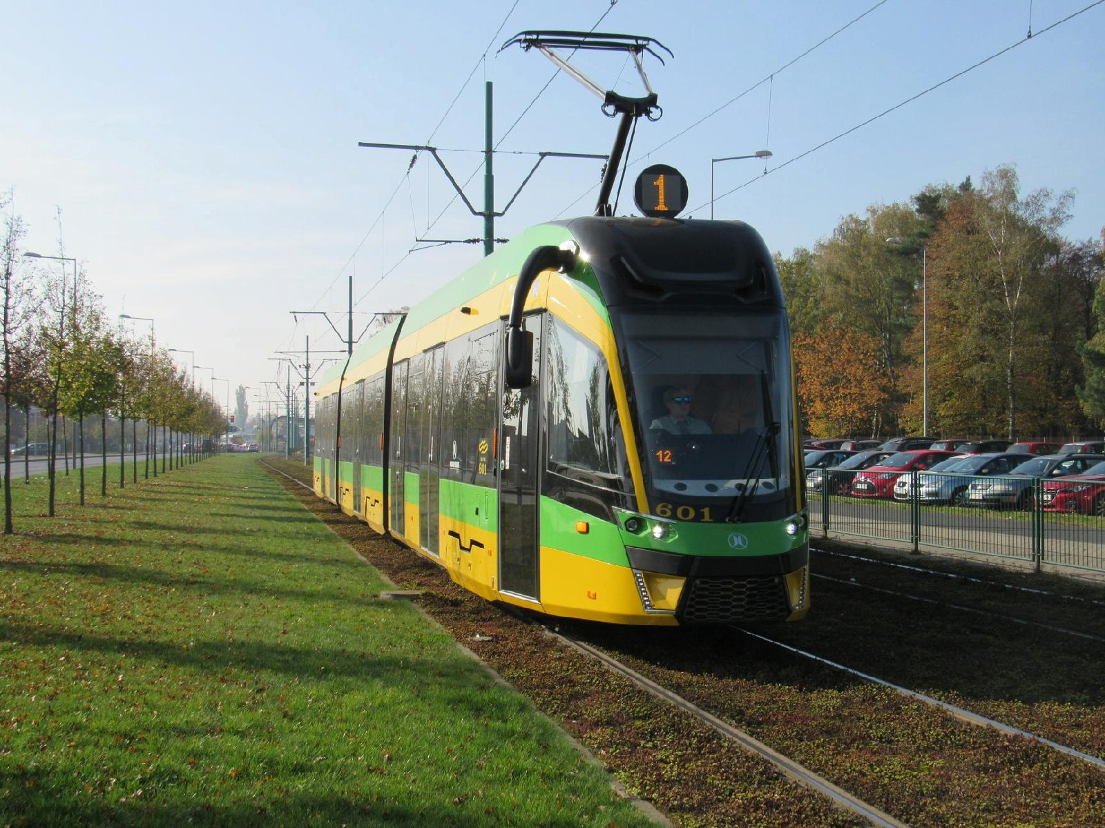 Żółto-zielony tramwaj linii nr 1 jadący z Junikowa, obok trawiasty pas zieleni