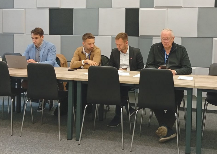 czterech mężczyzn siedzi za stołem w sali konferencyjnej - grafika artykułu