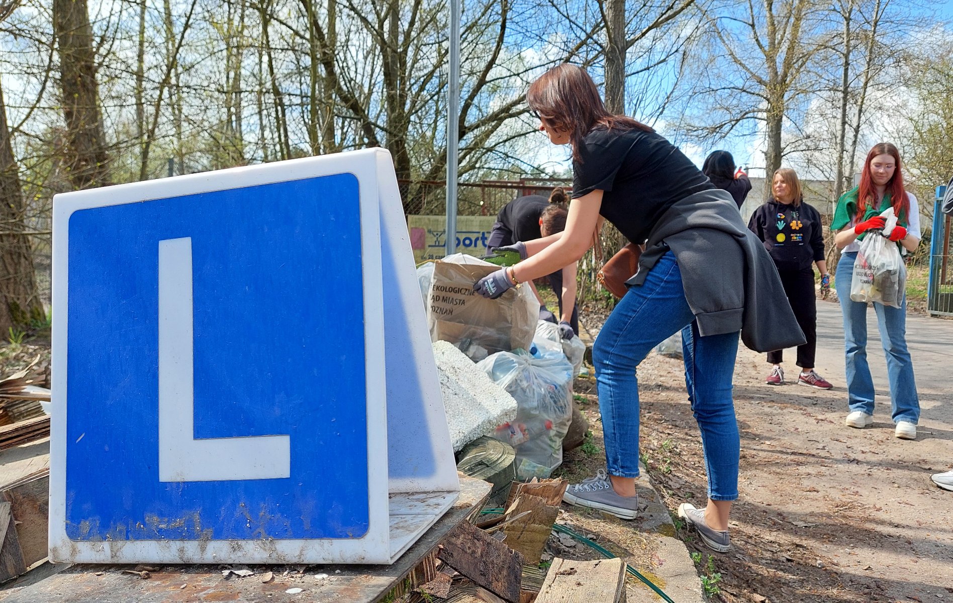 Na zdjęciu na pierwszym planie widać stos śmieci, stare palety, worki wypełnione odpadami. W tle stoi kilka osób